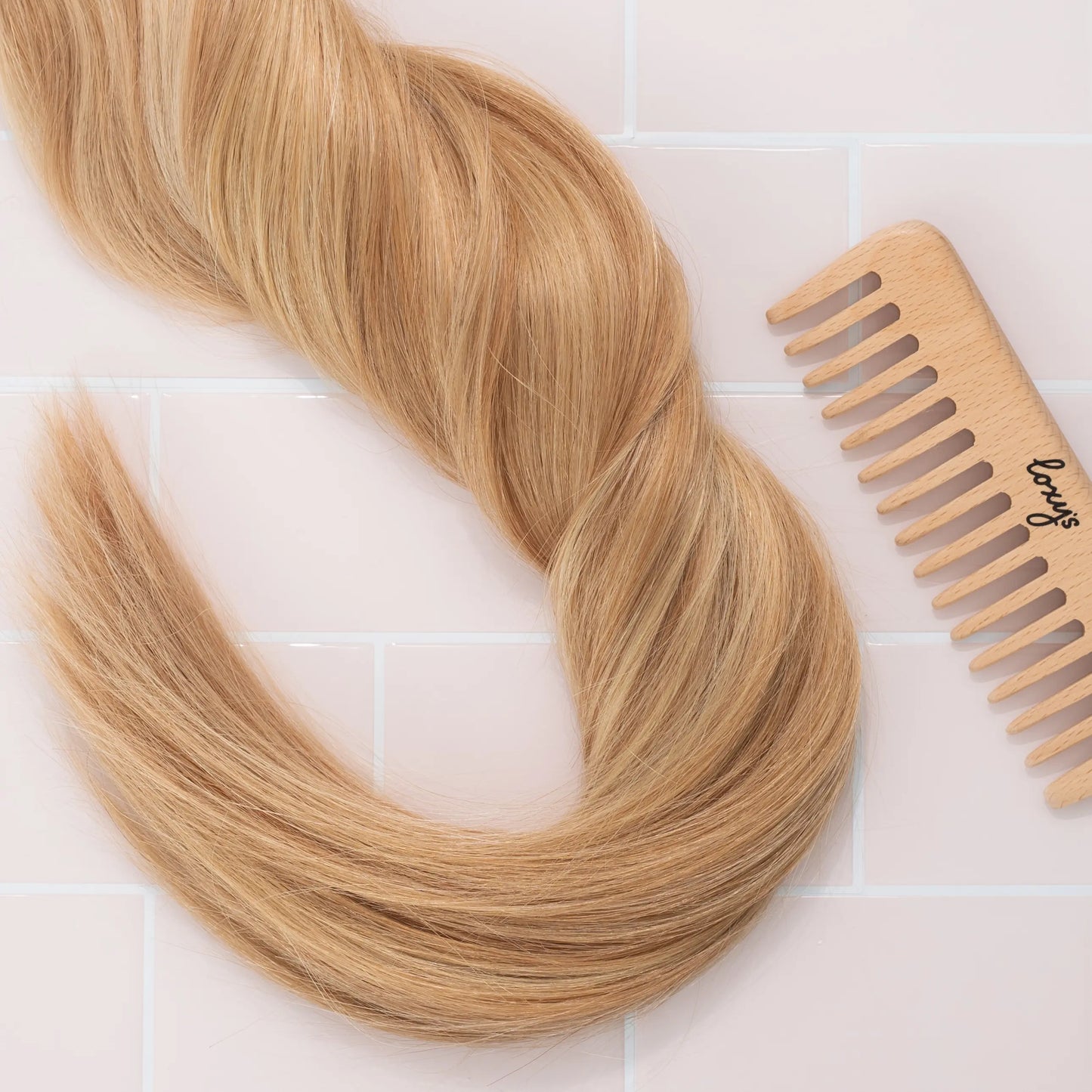 Boho hair extensions with a wooden comb on a light tiled background