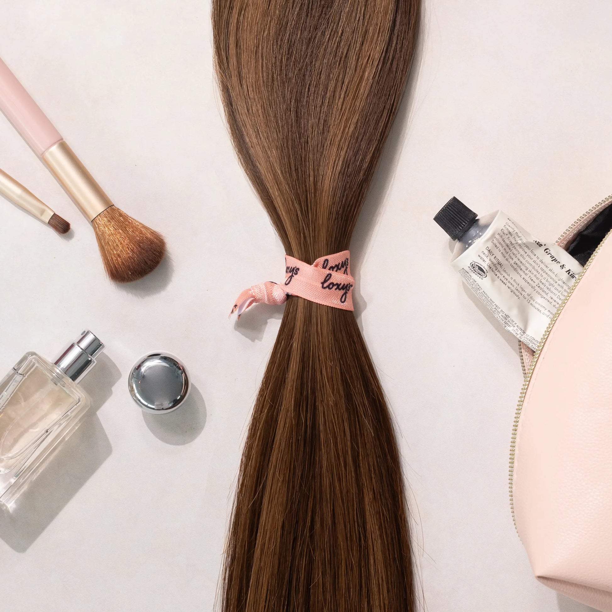 Loxys Java hair extensions on a white background with various beauty products laying around it